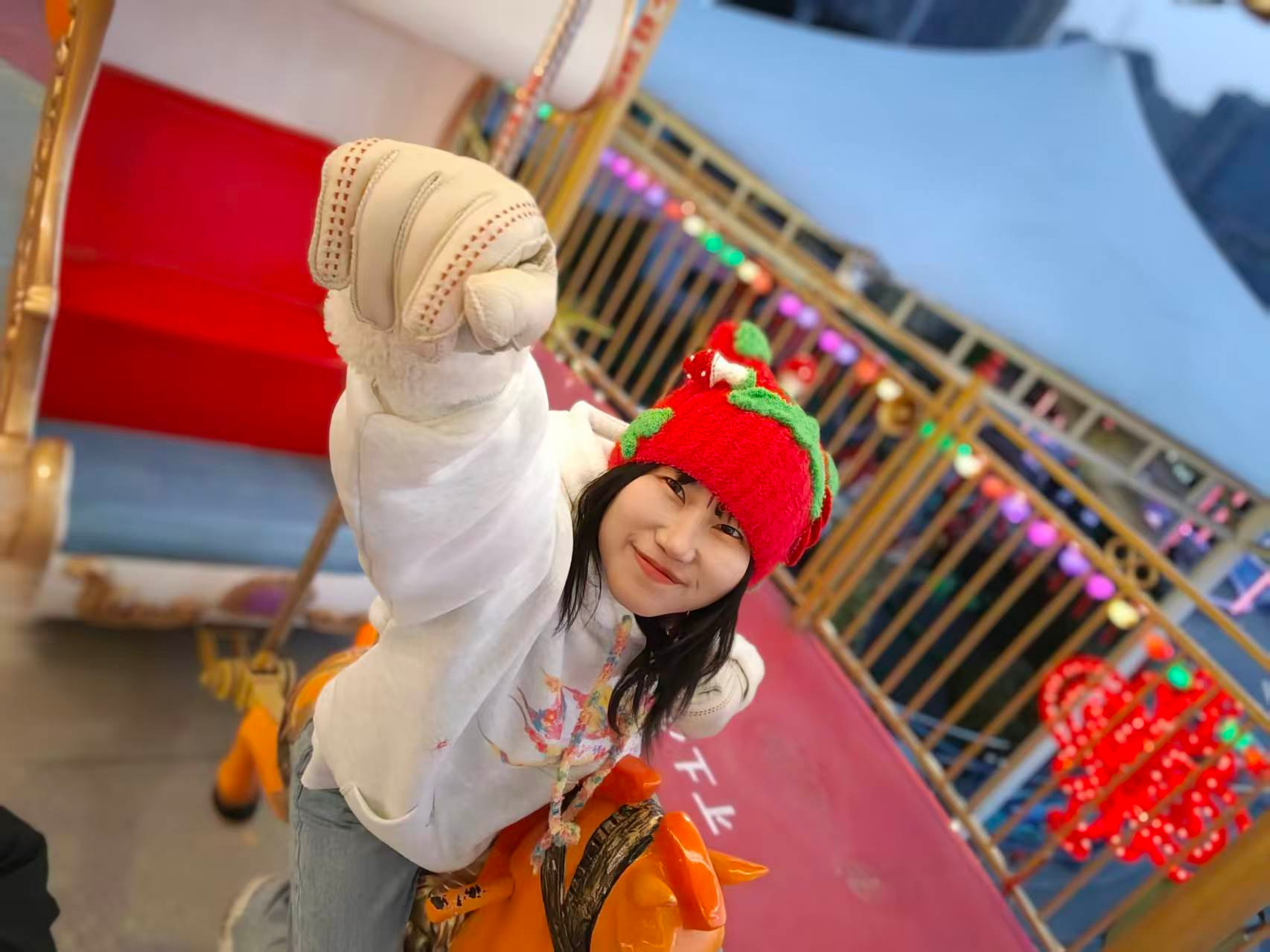 旋转木马上,戴红色毛线帽的女孩伸出拳头